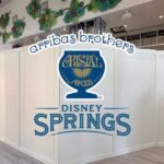 White temporary construction walls inside a Disney Springs retail store with an overlaid Arribas Brothers Cristal Arts logo.