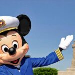 Captain Mickey Mouse waving in his nautical uniform in front of the Statue of Liberty to celebrate Disney Cruise Line sailing from New York City.
