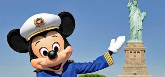Captain Mickey Mouse waving in his nautical uniform in front of the Statue of Liberty to celebrate Disney Cruise Line sailing from New York City.