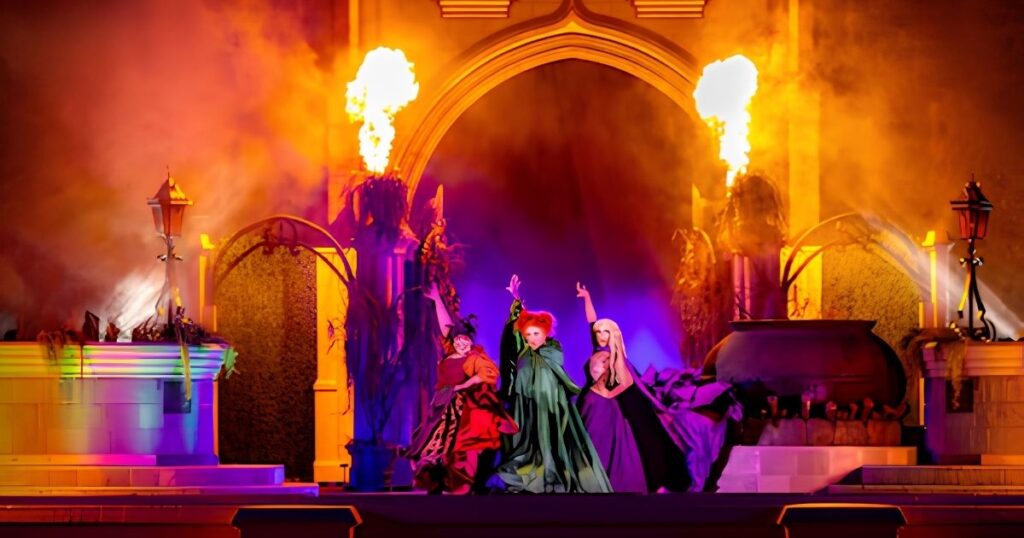 Mickey's Not-So-Scary Halloween Party 2026 7 The Sanderson Sisters performing on a vibrantly lit stage with fire effects and a cauldron during a Disney Halloween show.