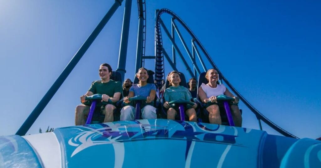 Guests smiling and riding the front row of the Mako hypercoaster at SeaWorld Orlando under a clear blue sky.