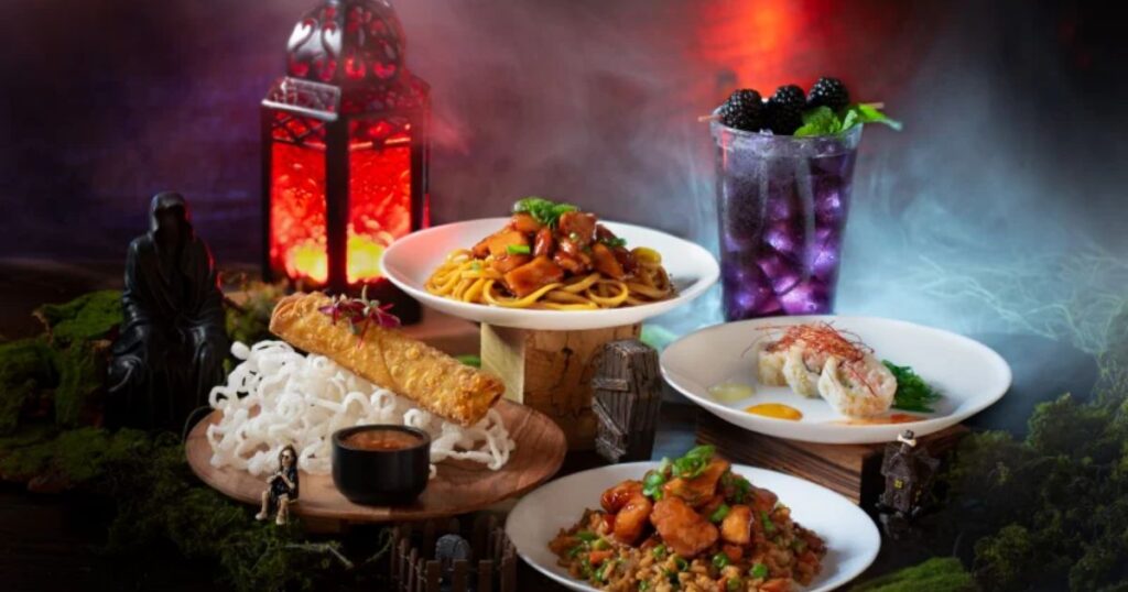 SeaWorld Orlando Spooktacular & Howl-O-Scream 2026 5 A spooky Halloween food and drink spread featuring noodles, a spring roll, fried rice, sushi, and a smoking purple cocktail decorated with small skulls and a glowing red lantern.