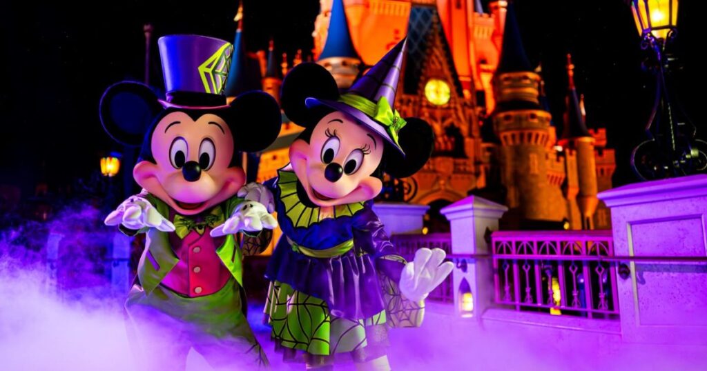 Mickey's Not-So-Scary Halloween Party 2026 4 Mickey Mouse and Minnie Mouse posing in Halloween costumes with purple fog in front of illuminated Cinderella Castle.