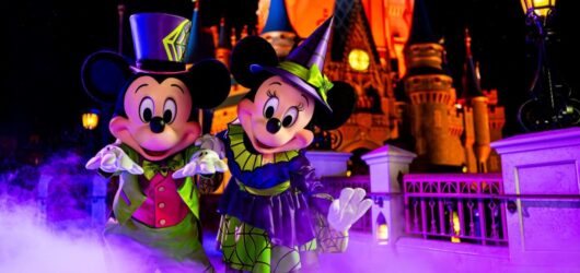 Mickey's Not-So-Scary Halloween Party 2026 25 Mickey Mouse and Minnie Mouse posing in Halloween costumes with purple fog in front of illuminated Cinderella Castle.