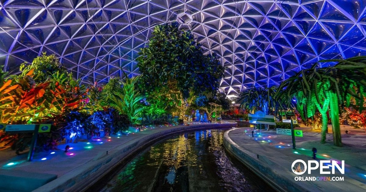 Waterway canal illuminated with colorful holiday lights inside EPCOT's Living with the Land greenhouse dome at night.