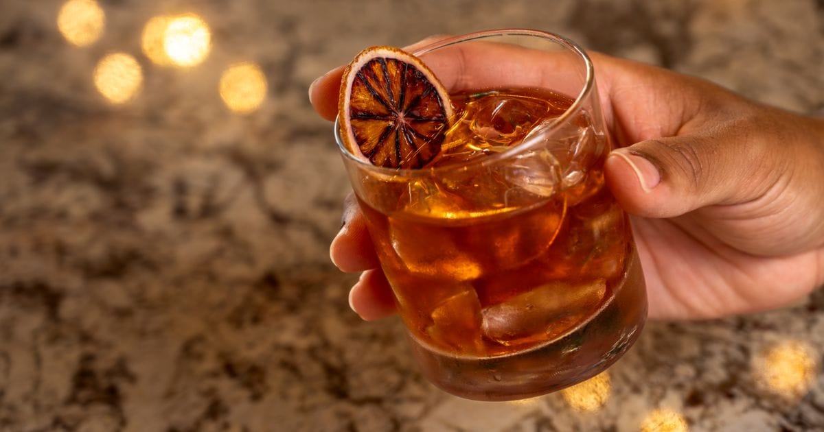 Handcrafted citrus Old Fashioned cocktail poured over ice in a rocks glass, highlighted by a charred dried fruit garnish