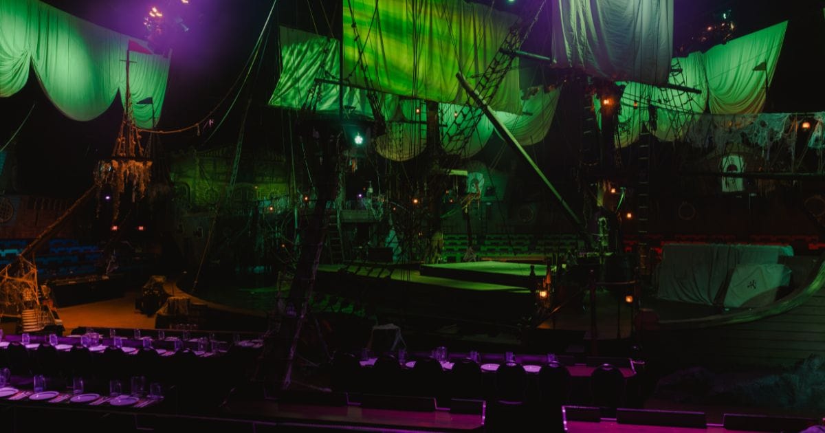 Indoor pirate ship arena lit in green and purple for the Vampirates dinner show with dining tables in the foreground