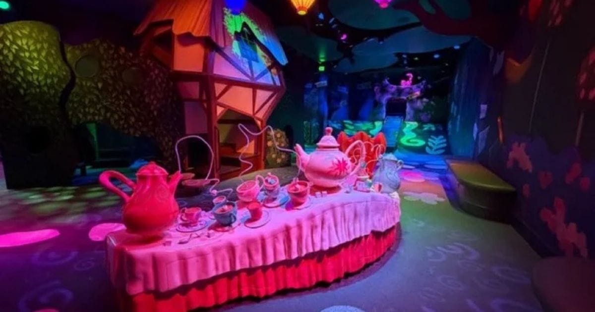 Indoor play area of Drawn to Wonderland showing the Mad Hatter tea party table with glowing teapots and Mary Blair treehouses