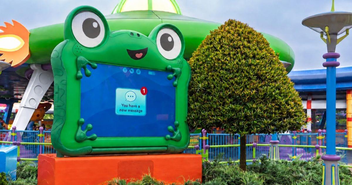 A green frog-shaped smart tablet prop named Lilypad, representing the new Toy Story 5 character, displays an unread message notification bubble in Toy Story Land at Disney's Hollywood Studios