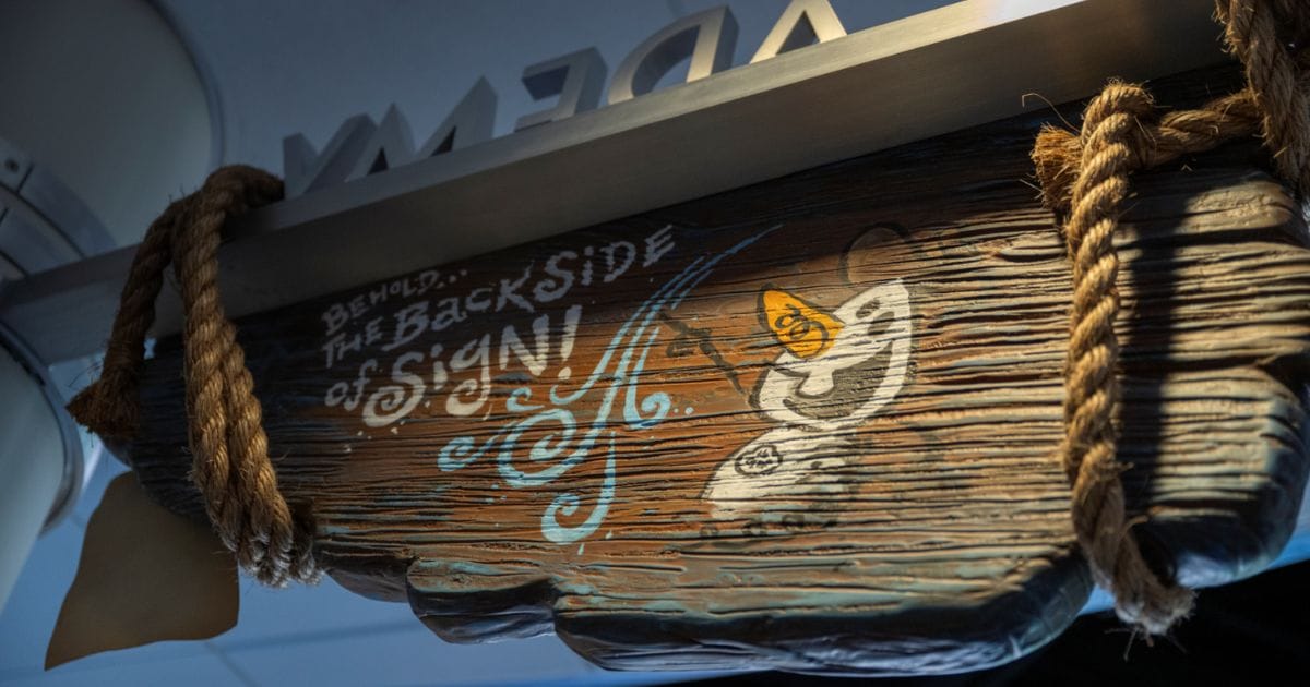Weathered wood sign reading Behold The Backside of Sign with a hand-painted sketch of Olaf