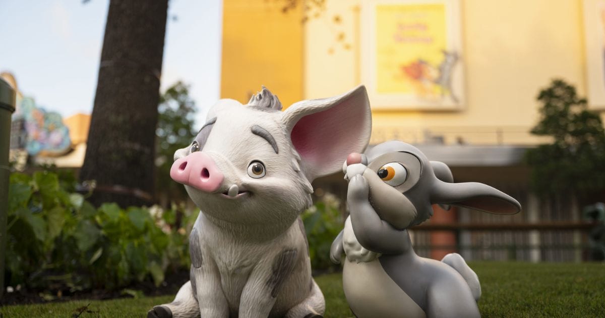 Sculpted figures of Pua from Moana and Thumper from Bambi sitting together in a grassy courtyard garden
