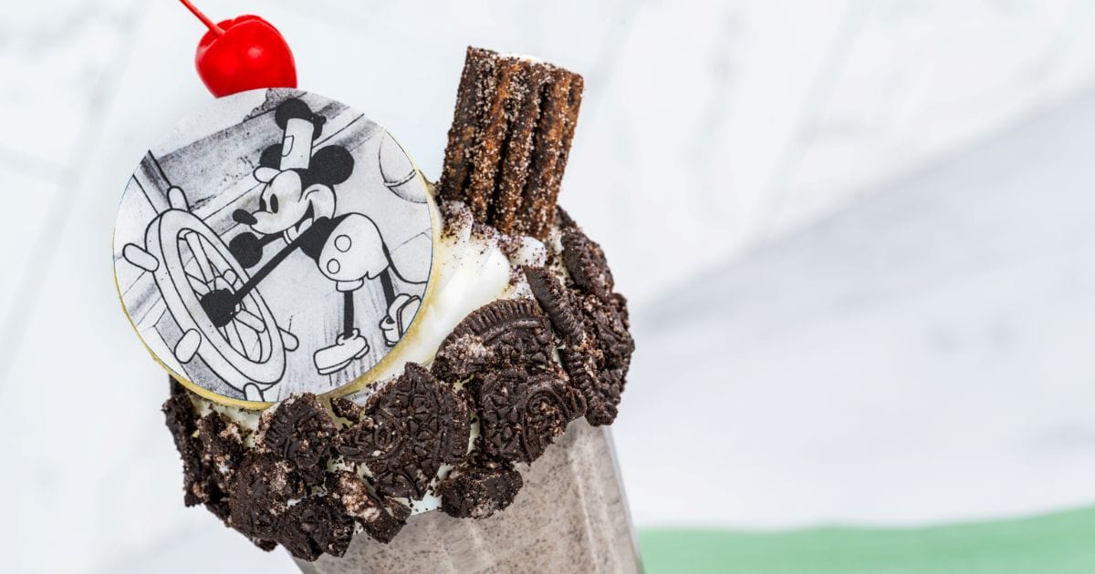 Over-the-top cookies and cream specialty shake featuring an Oreo crumb rim, cinnamon chocolate churro, bright red cherry, and classic Steamboat Willie chocolate disc