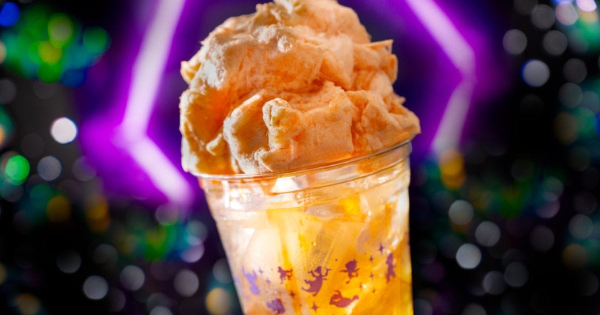 The Supernova Sip beverage in a clear glass with a swirl of orange cotton candy resting on the rim.
