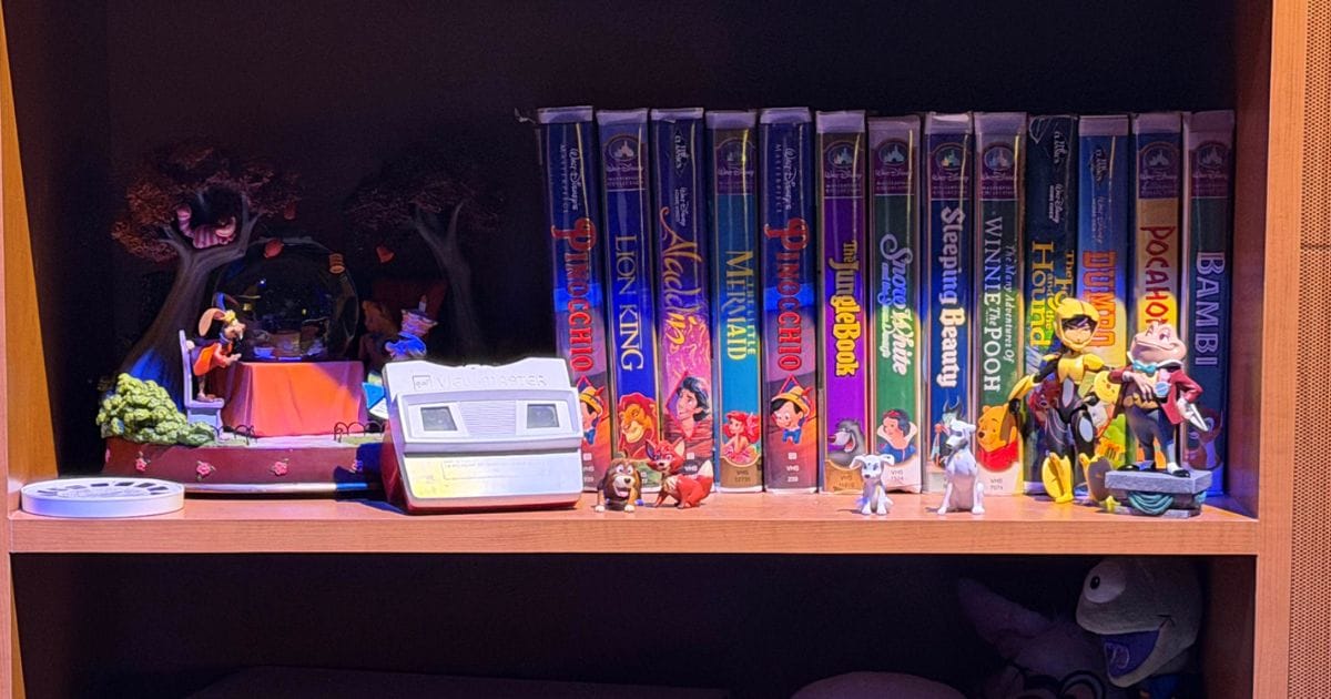 Themed studio shelf displaying vintage Disney clamshell VHS tapes, a View-Master, a Mad Tea Party snow globe, and character figurines