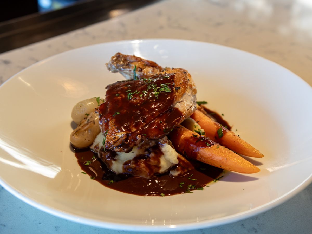 Savory Cocoa Coq au Vin plated with vegetables and chocolate demi-glace
