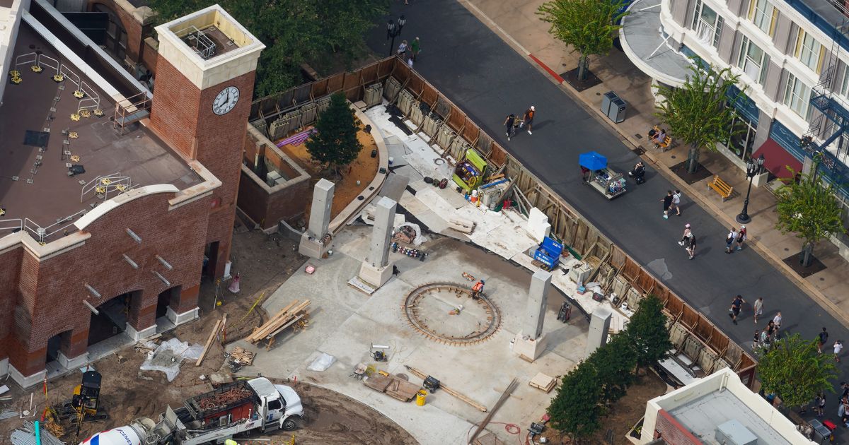 Freshly poured concrete and rebar with orange safety caps inside the central courtyard fountain base in front of The Glob Theater