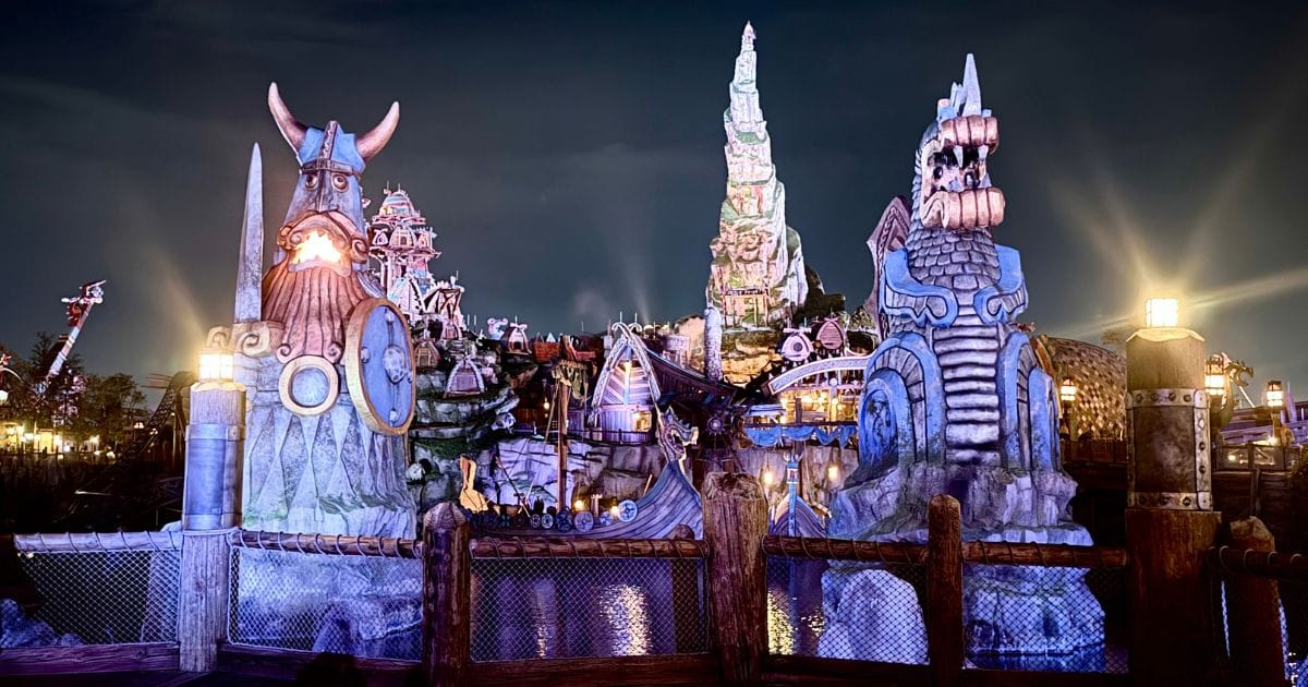 The glowing Viking statues and illuminated structures of the Isle of Berk reflecting in the water at night.