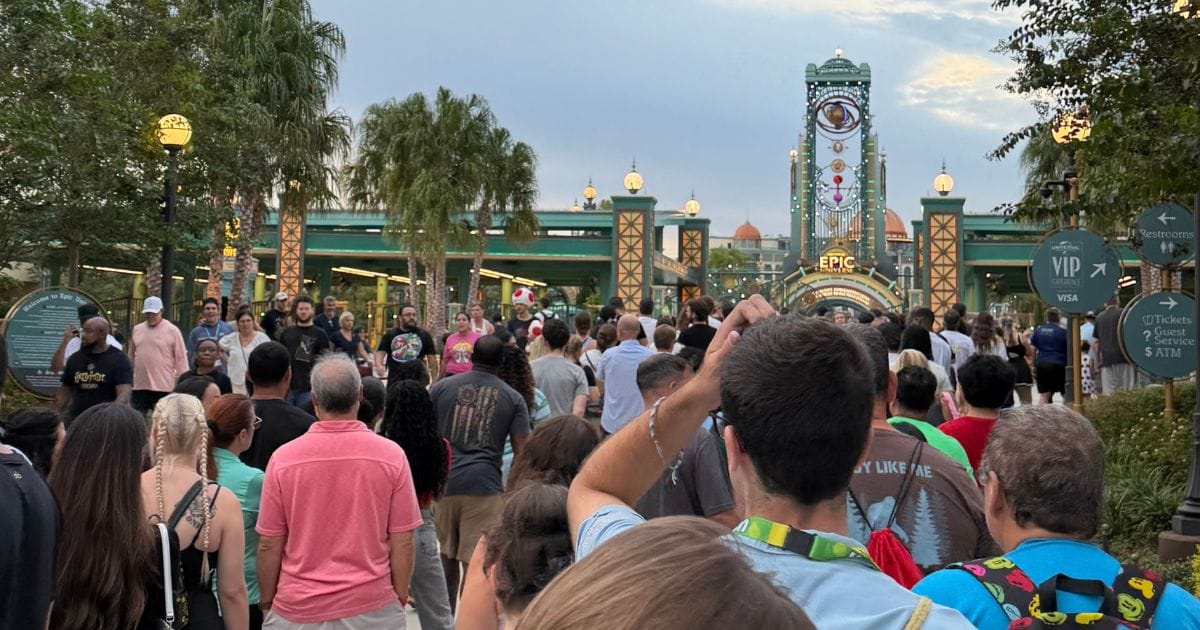 A crowd of guests waiting in line outside the Epic Universe entrance gates at dusk for the Universal Nights after-hours event.