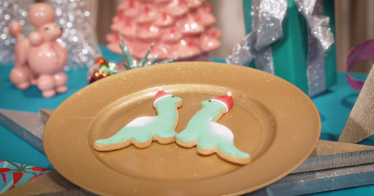 A shortbread cookie shaped like Gertie the Dinosaur wearing an icing Santa hat